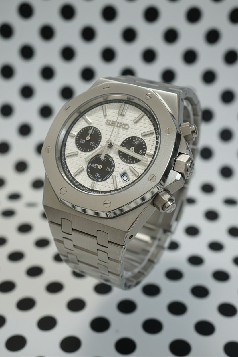 A stainless steel chronograph watch with an octagonal bezel, silver textured dial, and matching metal link bracelet, resting on a gray textured surface.