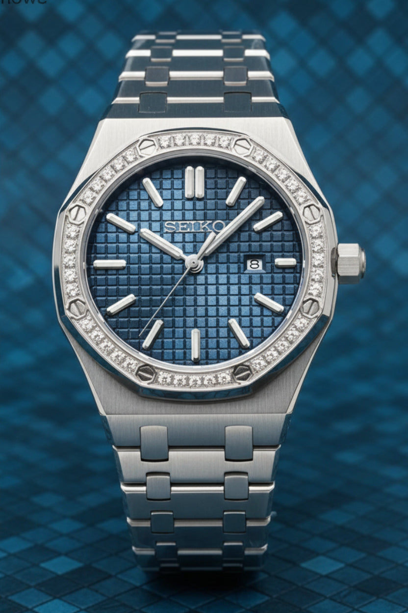 A silver-tone metal wristwatch with a textured blue dial and a bezel set with small clear stones, shown against a light gray background.