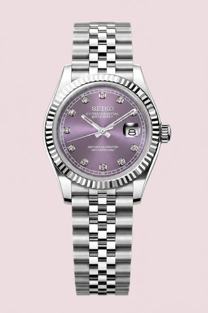 A Seiko wristwatch with a silver-tone stainless steel fluted bezel and link bracelet, featuring a lavender-purple dial with diamond hour markers and a date window.