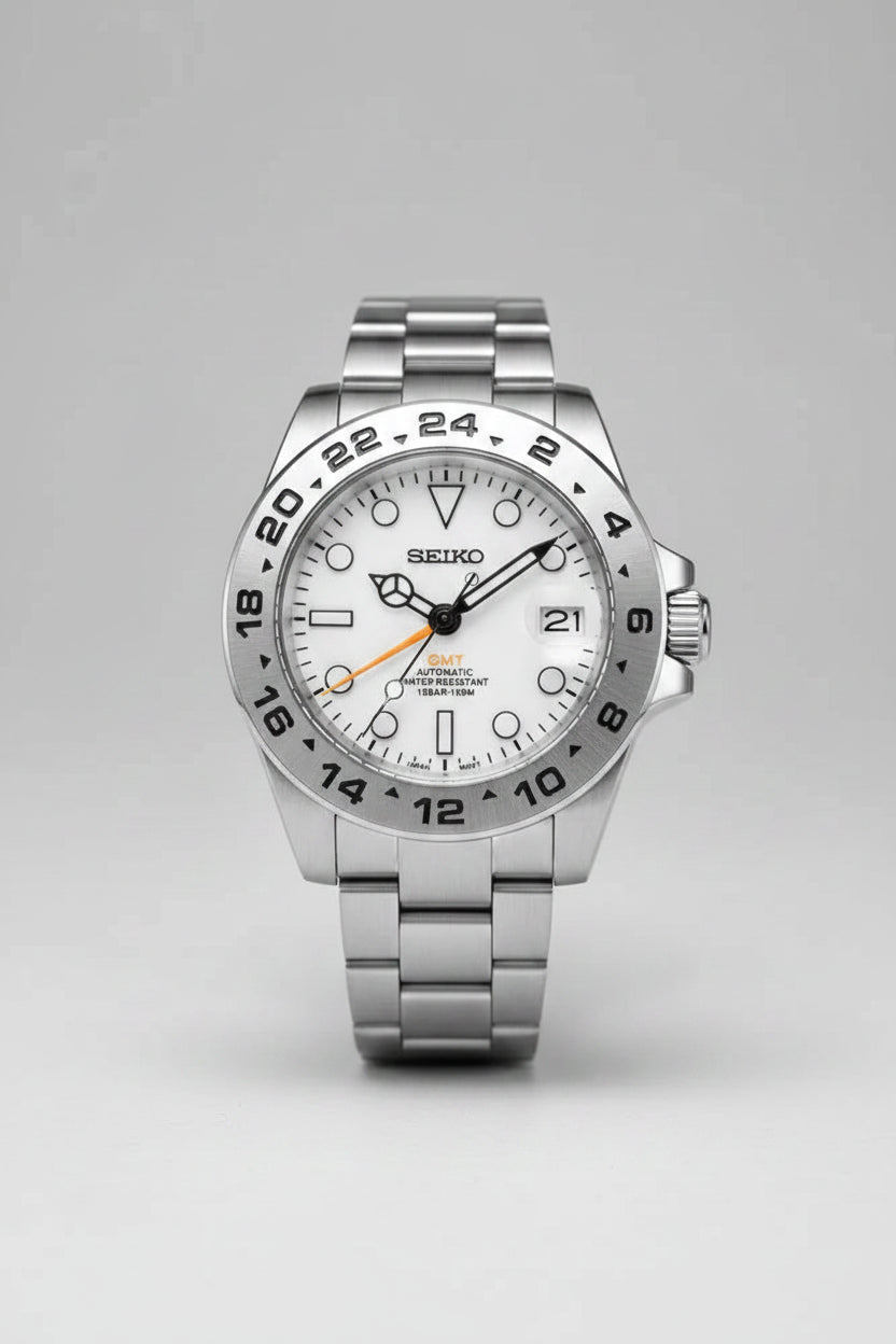 A Seiko stainless steel wristwatch with a silver-tone metal link bracelet, a white dial, and a black 24-hour bezel, shown against a solid black background.
