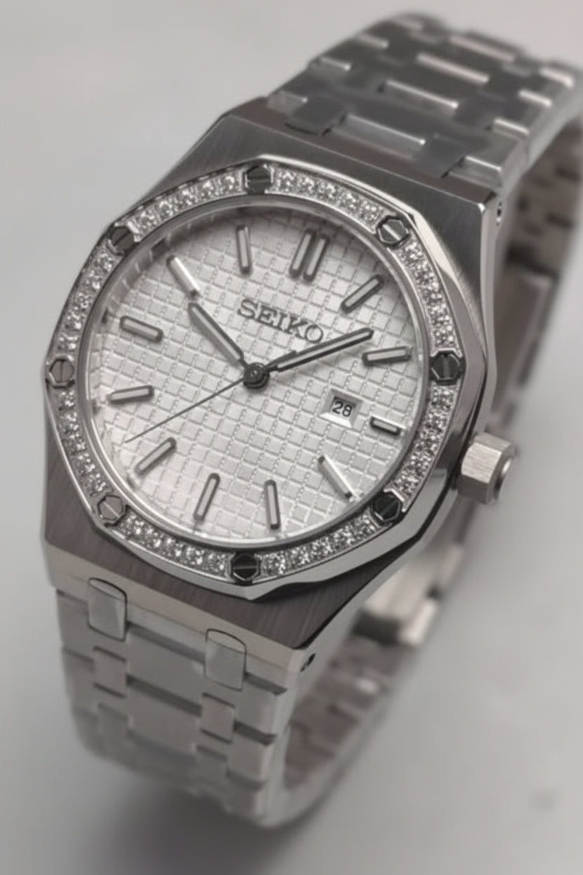 A Seiko stainless steel watch with a silver textured dial, a bezel set with small clear stones, and a matching metal link bracelet.