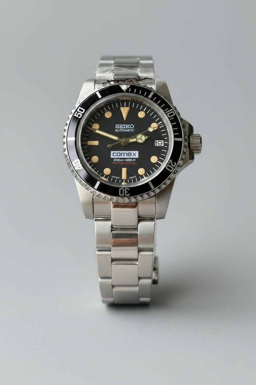 Silver Seiko watch with black dial held in a hand against a green leafy background