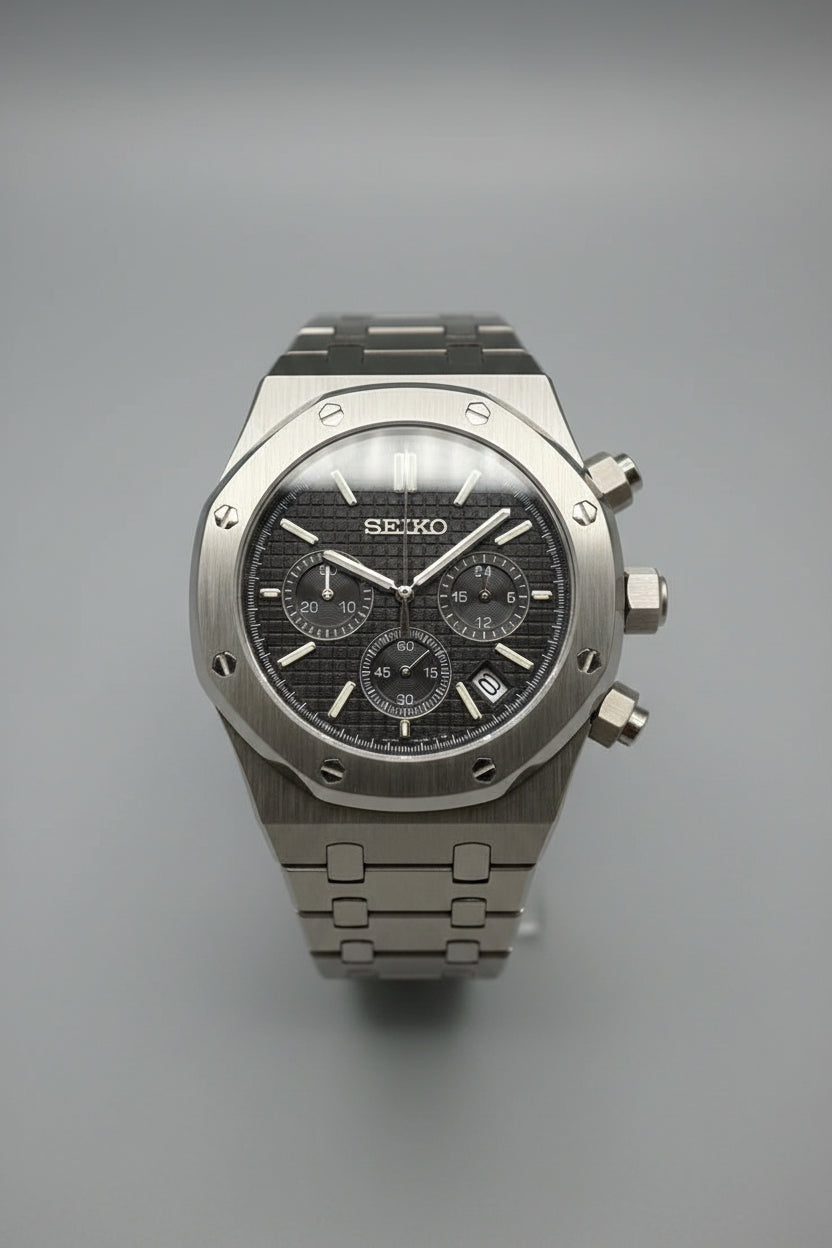 A Seiko wristwatch with a dark textured dial, a silver-toned metal case, and a matching metal link bracelet, photographed against a dark black background.