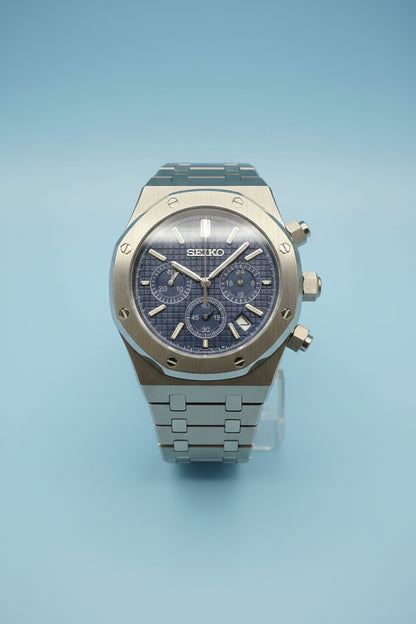 A Seiko Royal Oak chronograph watch with a blue dial and a silver-toned stainless steel case and bracelet, photographed against a dark gray background.