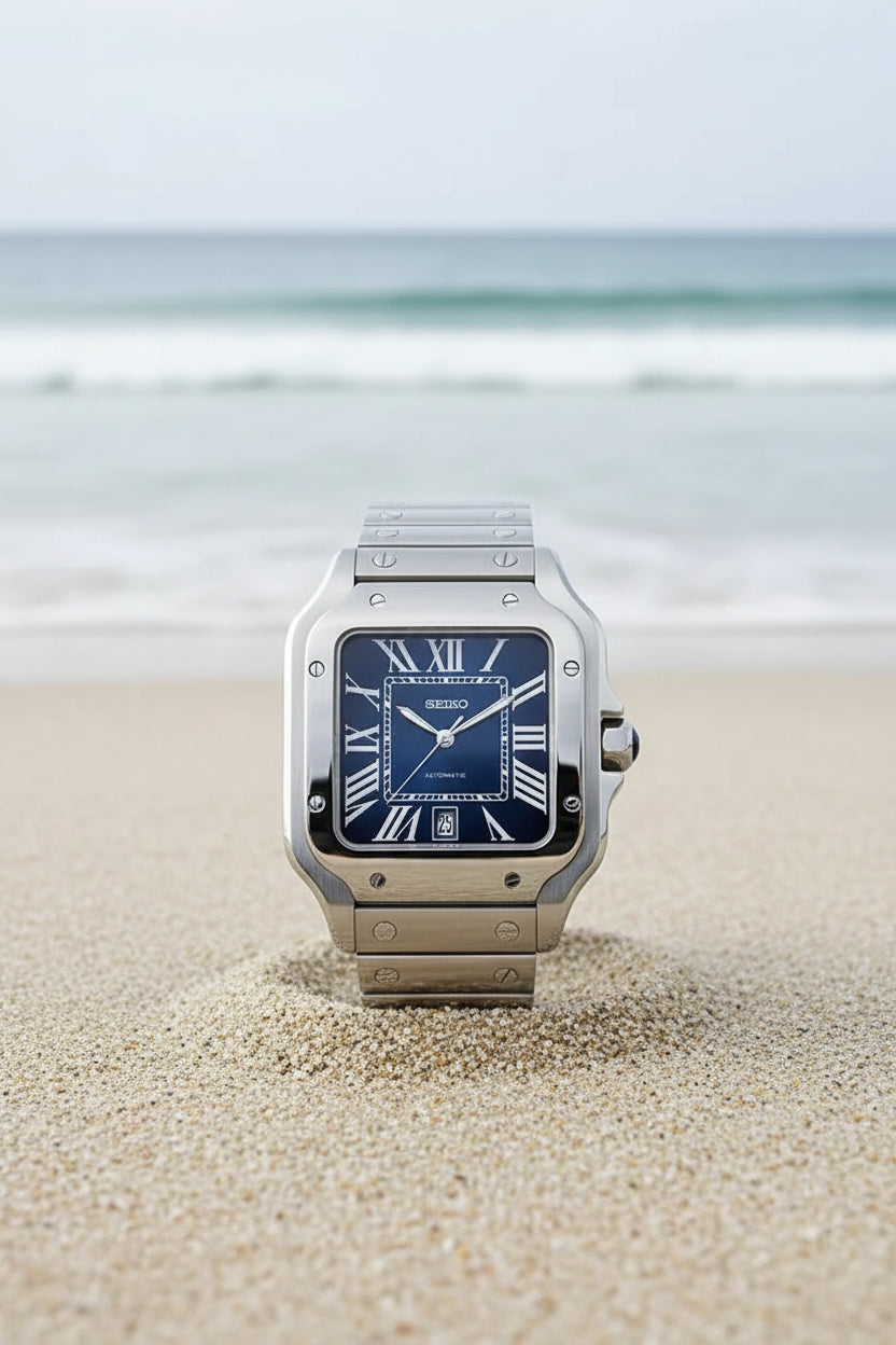 A Seiko watch with a silver-toned stainless steel case and integrated bracelet, featuring a dark blue dial with Roman numeral hour markers and a date window at the 3 o'clock position, set against a solid black background.