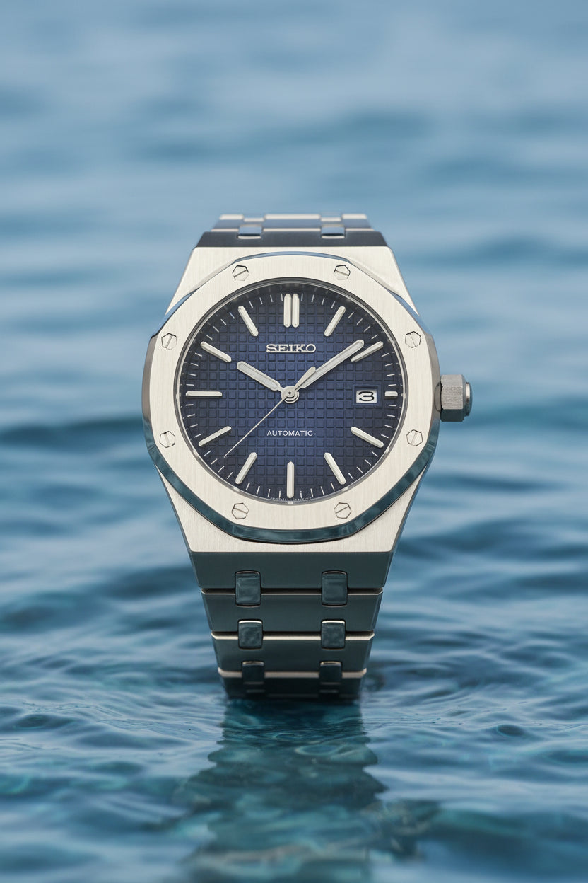 A Seiko automatic wristwatch with a brushed silver-tone metal case and integrated bracelet, featuring a textured dark blue dial with silver-tone indices and hands.
