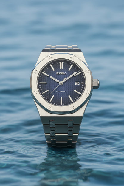 A Seiko automatic wristwatch with a brushed silver-tone metal case and integrated bracelet, featuring a textured dark blue dial with silver-tone indices and hands.