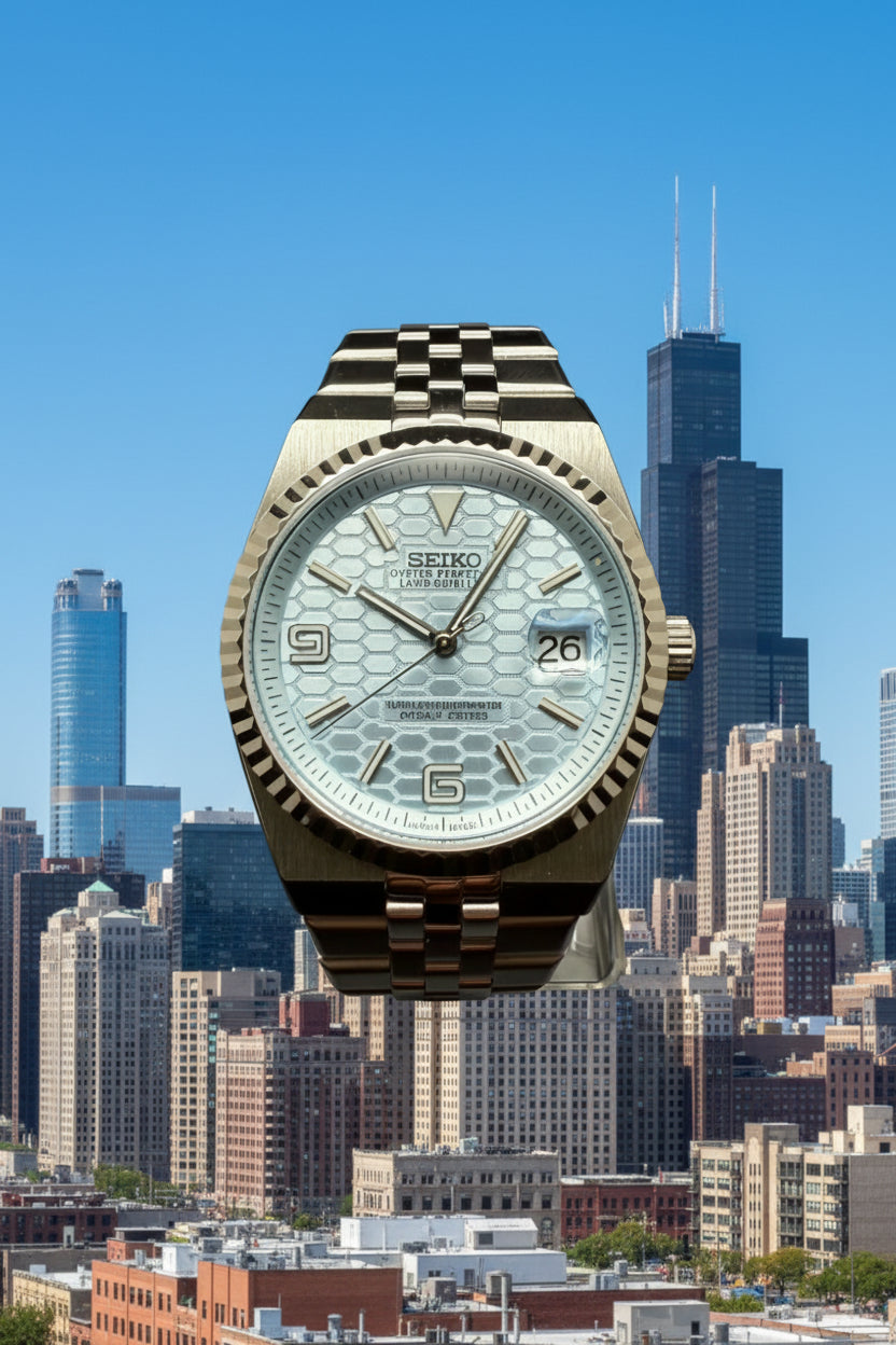 A Seiko stainless steel watch with a light blue dial and a checkered metal bracelet, displayed on a stand against a dark background.