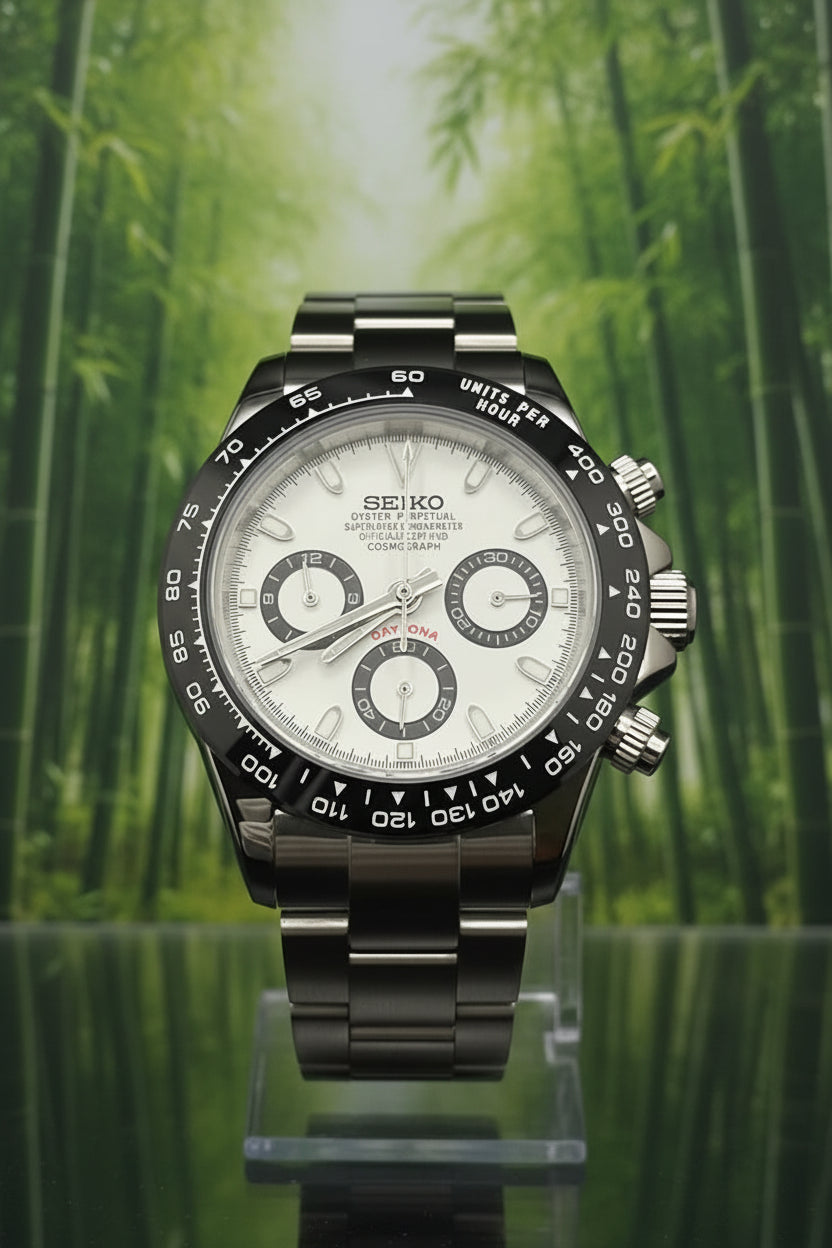 A Seiko Daytona watch with a silver stainless steel case, white dial, and black tachymeter bezel, displayed on a clear stand against a black background.