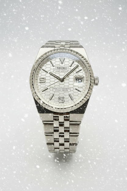 A Seiko stainless steel wristwatch with a textured silver dial, fluted bezel, and matching steel link bracelet, photographed against a dark gray background.